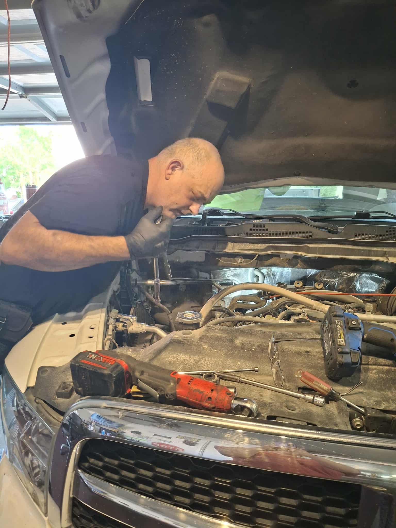Mechanic leaning under an open hood working on an engine with tools staged